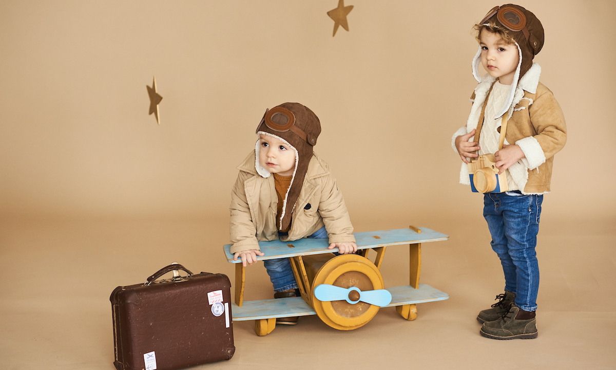 two brothers are played with a toy airplane and a suitcase on a beige background. dreams and travel concept