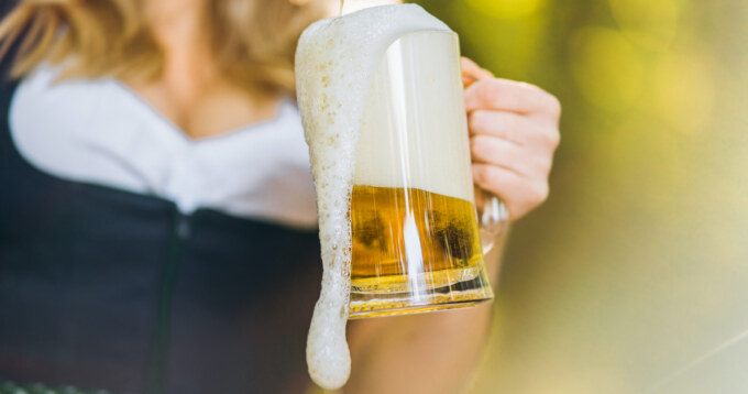 Close-up of the girls hands in dirndl pouring a full glass of beer with huge foam outdoors