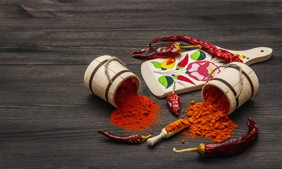 Magyar (Hungarian) red sweet and hot paprika powder. Traditional pattern on a cutting board, different varieties of dry pepper. Black wooden background